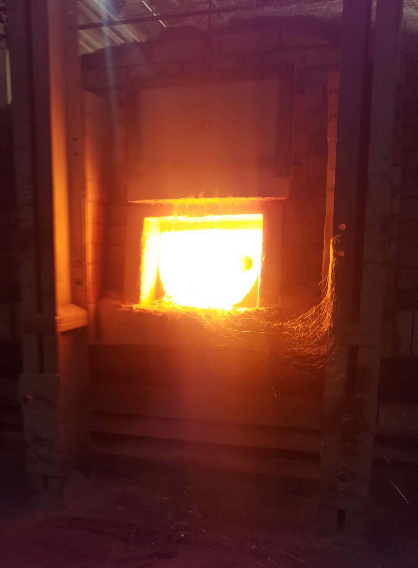The fiery glow of a furnace lighting a dark room—where molten glass begins its journey into stained glass art.